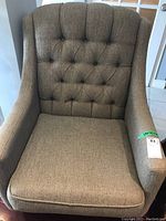 Front view of the brown upholstered arm chair with tufted backrest and removable seat cushion on tiled floor near a door.