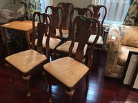 Six wooden dining chairs arranged together, showing two with arms and four armless, light upholstery and dark wood finish.