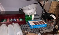Shelf showing 4 clear ice cube holders with lids, white colander, Pyrex measuring cup, condiment bottles, poker chip set in wooden case.