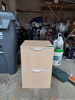 Front view of a laminated filing cabinet with 2 drawers in a garage setting, showing the light wood finish and built-in handles.