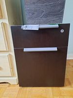 Front view of wood filing cabinet showing two drawers, dark brown front with silver handles, white sides, and the round lock hole on top drawer missing key.