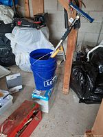 Photo showing two stacked blue Lowe's buckets with cleaning brush and squeegee inside, red toolbox on floor nearby, garage setting