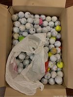 Top view of the box filled with numerous golf balls including white, yellow, and a few with colored markings.