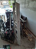 Aluminum 4ft ladder folded, standing against a wall with other items nearby including a golf bag and some wood pieces.
