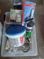 Overview of lot showing light switches, drywall compound tub, flush valve, tape measure, and plumbing parts.