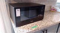 Panasonic The Genius NN-SU65LB microwave oven in black on granite counter with visible control panel.