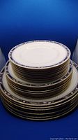 Stack of plates showing varying sizes including dinner, salad, and bread plates with blue, gold, and pink floral borders on white porcelain.