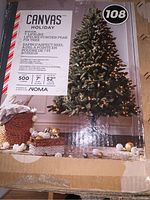 Box front showing Canvas Holiday brand, 7 feet height, 52 inch diameter with 500 pre-lit NOMA lights on a lifelike white powder-flecked fir tree.