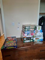 Stack of more than 10 boxes of 1000-piece puzzles on a wooden dresser.