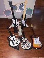 Five guitar controllers arranged around electronic drum set on wood floor