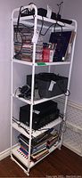 Full view of white coated metal shelving unit filled with various items including electronics, DVDs, and books, showing unit structure and shelves.