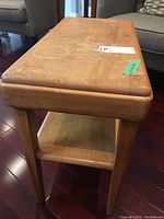 Photo showing the wood side table from a front angle, displaying the damaged finish on the top surface and the lower storage shelf.