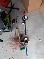 Overview of the lot showing the Black & Decker trimmer, metal shovel, and leaf rake on a concrete floor.