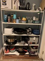 Utility shelf loaded with kitchenware including toasters, pots, pans, bowls, plates, and containers for scale and context.