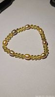 Full view of the gemstone and pearl bracelet on a white surface showing alternating citrine faceted beads and gold pearls.