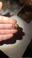 Front view of the pair of amethyst drop sterling silver earrings held between fingers under direct light showing color and size.