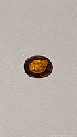 Photo of an oval cut natural zircon gemstone with deep electric orange color on a white background, showing color and cut details.