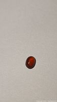 Deep orange hessonite garnet gemstone viewed on a flat surface showing its oval cabochon shape and polished finish.