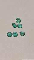 Six natural emerald gemstones spread out on a flat surface showing their green coloration and oval shape.