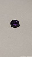 Oval cut deep purple amethyst gemstone lying flat showing shine and clarity.