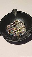 Photo shows a black container holding numerous tiny multi-colored faceted gemstones approximately 1-2 mm each.