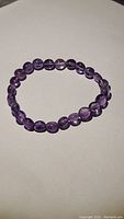Full view of the amethyst bead bracelet arranged in a circular shape on a flat surface.