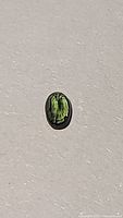 Bright green oval-shaped sapphire gemstone placed on a neutral background to show color and clarity.
