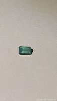 Close-up photo of a rectangular emerald cut green gemstone placed on a neutral surface.