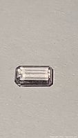 Rectangular emerald cut natural kunzite gemstone showing facets, off-white with light pink hue