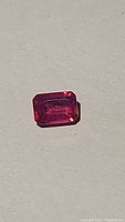 Close-up photo of an emerald cut hot pink reddish natural ruby with good luster on a plain background.