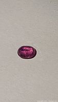Oval cabochon natural ruby showing deep pink-red color, clarity enhancements visible internally, polished surface, approximately 8.8x6.9mm size.