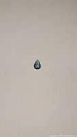 Pear shaped paraiba blue tourmaline gemstone on a plain background, showing size and color.
