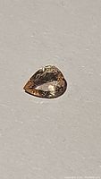 Close-up photo of a pear cut natural pink tourmaline gemstone displaying soft pink to peach color on a plain grey background.