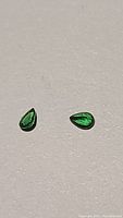 Two loose pear-shaped green tsavorite garnet stones on a flat neutral surface