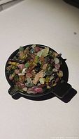 Small parcel of assorted natural rainbow tourmaline crystals in a black dish showing variety of colors and shapes.