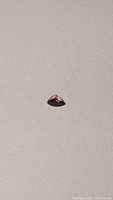 Top and angled view of small trillion cut deep purple red sapphire gemstone on light background.