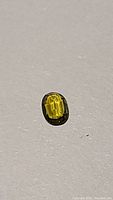 Single oval-cut yellow green tourmaline gemstone placed on a white background displaying clarity and color.