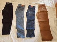 Photo showing four pairs of men's jeans laid flat: black Levi's Silvertab, light blue Lucky Brand, medium blue Levi's 501, and brown Carhartt workwear jeans.