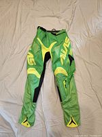 Front view of neon green Alias men's motocross pants laid flat on a light surface, showing color details and branding clearly.