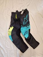 Alpinestars Techstar Screamer men's moto pants laid flat on white surface showing front and leg details including multicolor accents and tags attached.