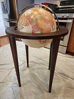 Full view of the floor standing globe showing its dark wood stand, cylindrical legs, and antique-style globe with metallic semi-meridian ring.