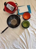 Photo showing two large red plastic colanders, one KitchenAid brand, three green silicone bowls of different sizes, two Michael Graves silicone bowls (orange and purple), nonstick 14 inch wok, one wooden cutting board, two plastic cutting boards (white and blue), and a box grater.