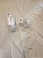 Photo showing white Hamilton Beach hand mixer with storage case and white Black & Decker mini food processor with cord on fabric surface.