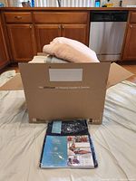 Box open with towels visible inside and new packaged item beside the box on a bed