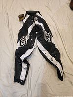 Photo of black and white Troy Lee Designs SE Air MX men's motocross pants laid flat, showing front side and layout of graphic details and logos.