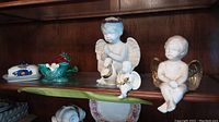 Ceramic angels sitting and praying arranged on wooden shelf, largest angel about 9 inches tall