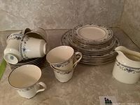 Dish set arranged with stacked plates, cups, and cream pitcher showing floral blue pattern and gold trim