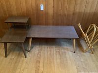 Overall view of vintage coffee table, 2-tier end table, and folding magazine rack against wood-paneled wall and hardwood floor