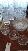 Full view of crystal serveware and vases on wooden table showing multiple bowl sizes and two tall vases with cut patterns