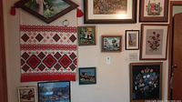 Overview of multiple framed needlepoint artworks and a Ukrainian hanging textile with geometric embroidery on the wall.